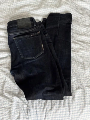 Mörkblå jeans från Neuw, model ”Iggy skinny” 31/32 - Säljer ett par mörkblå jeans från Neuw med klassisk femficksmodell och raka ben. Jeansen har en diskret logga på bakfickan och är tillverkade i ett slitstarkt denimtyg. Perfekta för dig som gillar stilrena och tidlösa jeans.