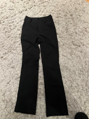 Svarta kostymbyxor från Bik Bok - Säljer ett par svarta kostymbyxor från Bik Bok med klassisk rak passform. Byxorna har diskreta fickor och stängs med dragkedja och knapp. Perfekta för en stilren look.