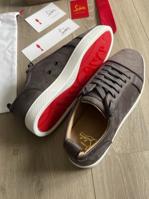 Gråa sneakers från Christian Louboutin - Snygga gråa sneakers i mocka från Christian Louboutin med klassisk röd sula och vita kanter. Skorna är helt nya aldrig använda 10/10 skick. Alla tillbehör ingår. Storlek 44. Pris kan diskuteras vid snabb affär 