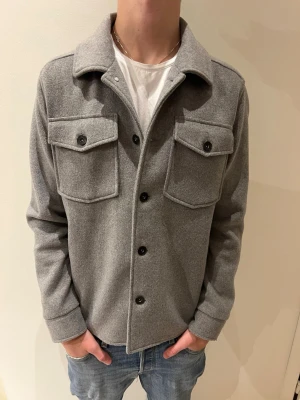 Grå Hampton Republic Overshirt - Stilren grå Hampton Republic overshirt med klassisk krage och fyra knappar framtill i storlek S