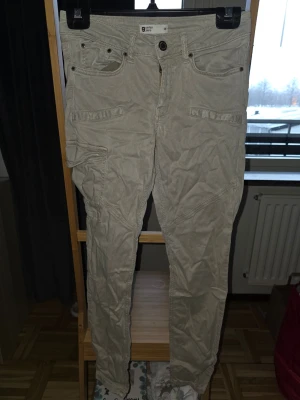Beige cargobyxor från Garden Jeans - Säljer ett par beige cargobyxor från Garden Jeans med flera fickor och detaljerade sömmar. Byxorna har klassisk cargomodell med fickor på sidorna och fram, samt knapp och dragkedja i midjan. Perfekta för en avslappnad och trendig stil.