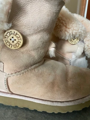 Äkta uggs  - Äkta australian uggs i fint skick, ljusrosa med nedvikbar kant. De har vintage träknappar på sidorna och är väldigt gosiga. De är i äkta läder och äkta ull, säg till om du vill ha fler bilder/ bild på! De har ett litet hål på framsida vänster sko