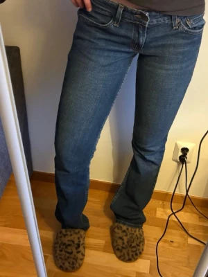 Blå bootcut jeans med låg midja - Snygga blå bootcut jeans med låg midja och klassiska fem fickor. Jeansen har en lätt tvättad look och raka ben som går ut lite nedtill. Perfekta till en avslappnad stil och passar till det mesta. Inget synligt märke på jeansen.
