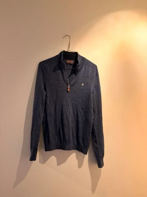 Mörkblå halvzip tröja från Morris  - Klassisk mörkblå stickad tröja från Morris med halv dragkedja och liten broderad logga på bröstet. Tröjan har ribbade muddar och krage, perfekt för en stilren och avslappnad look. Materialet känns mjukt och bekvämt. 100% Merino wool 