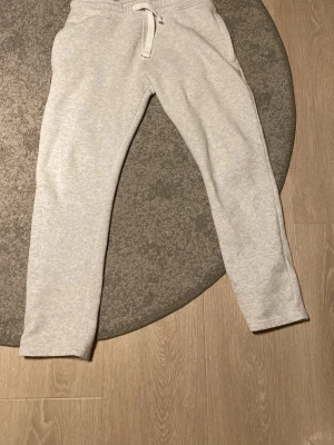 Ljusgrå mjukisbyxor med dragsko - Säljer ett par ljusgrå mjukisbyxor med dragsko i midjan. Byxorna har sidofickor och är tillverkade i mjukt, bekvämt material som passar perfekt för chill dagar. Klassisk rak passform och enkel design.