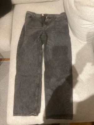 Svarta loose fit jeans från H&M - Säljer ett par svarta loose fit jeans från H&M med justerbar midja. Klassisk femficksmodell i denim med raka ben och knappgylf. Perfekta för en avslappnad och trendig look.