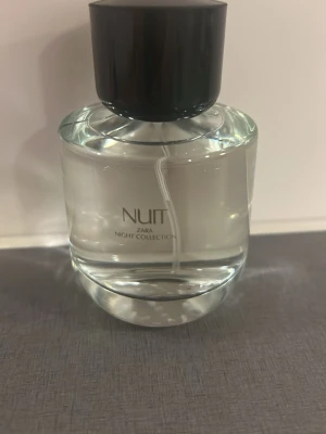 Zara Nuit Night Collection parfym - Zara Nuit Night Collection parfym i en rund, genomskinlig glasflaska med svart lock. Flaskan har en stilren och modern design med enkel text på framsidan. Perfekt för dig som gillar eleganta och minimalistiska doftflaskor.