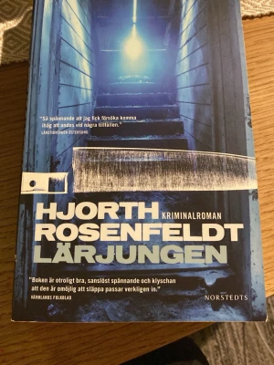 Lärjungen av Hjorth & Rosenfeldt - Säljer kriminalromanen 'Lärjungen' av Hjorth & Rosenfeldt. Boken har ett blått omslag med motiv av en trappa och en stor kniv, och är utgiven av Norstedts. Perfekt för dig som gillar spännande och actionfyllda deckare. Storpocket 