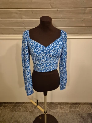 Blå blommig croppad topp - Blå croppad topp med vita små blommor och långa ärmar💙🌼 Supersöt och perfekt till sommaren. Knappt använd. Man kan ha den off shoulder också. Det är bara att skriva om man har frågor!😊💖