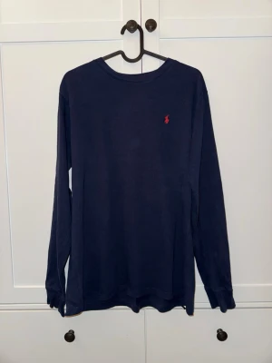 Mörkblå långärmad tröja Polo Ralph Lauren - Mörkblå långärmad tröja från Polo Ralph Lauren med rund halsringning och den klassiska röda logotypen broderad på bröstet.