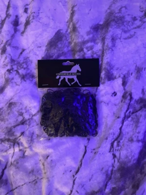 Svarta gummiband Copperfield Access - En förpackning med svarta gummiband från Copperfield Access. Gummibanden är små, runda och tillverkade i elastisk plast. Perfekta för att använda till hästflätning, pyssel eller andra kreativa projekt där små gummiband behövs.