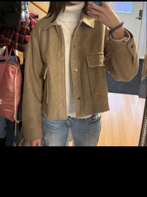Beige overshirt med stora fickor - Snygg beige overshirt i ullmix med krage och stora bröstfickor. Rak, boxig passform och knäppning framtill. Perfekt att slänga över en hoodie eller polotröja för en chill look. Passar till jeans eller kjol för en trendig vibe. Står att tröjan är XL men passar mig med xs/s