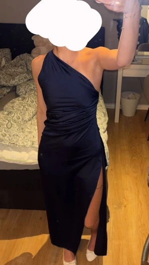 Marinblå balklänning  - Snygg marinblå balklänning med oneshoulder-design och hög slits på sidan. Klänningen har en elegant drapering och smal passform som framhäver figuren. Storlek S och aldrig använd!