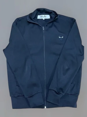 Zip  Play Comme des Garçons - Svart hoodie med dragkedja från Comme des Garçons PLAY. Liten hjärtlogga med ögon på bröstet och stor hjärtformad logga med ögon på ryggen. Mjuk bomullskänsla och ribbade muddar. Perfekt för en stilren och cool look.