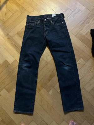 Svarta raka jeans från Levi's - Säljer ett par svarta raka jeans från Levi's med klassisk femficksdesign och knappgylf. Jeansen har en stilren look och är tillverkade i kraftig denim. Perfekta för dig som gillar en tidlös och enkel stil.