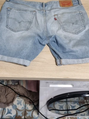 Levi's 501 CT ljusblå jeansshorts - Ljusblå jeansshorts från Levi's modell 501 CT med klassisk femficksdesign och uppvikta benslut. Ikonisk läderpatch bak och röd Levi's-tagg på fickan. Perfekta för en avslappnad och cool stil.