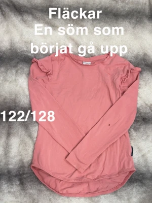 Rosa långärmad topp med volang - Söt rosa långärmad topp från Polarn o pyret med volangdetaljer på axlarna. Rund halsringning. Perfekt till jeans eller kjol för en avslappnad look.🌸 Fläckar. Storlek 122/128