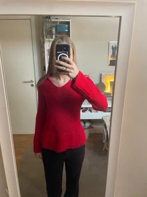 Röd stickad tröja med v-ringning - Snygg röd stickad tröja med v-ringad hals och breda ribbade muddar. Tröjan har en lätt utsvängd nederkant och är perfekt för dig som vill ha en färgklick i garderoben. Materialet känns mjukt och bekvämt, och modellen är lite figurnära.