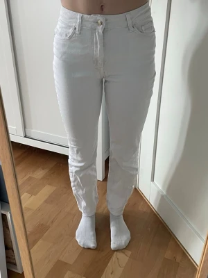Lätt utsvängda jeans med hög midja - Säljer ett par vita jeans med hög midja. Jeansen har klassiska fem fickor, gylf med dragkedja och knapp samt bälteshällor. Materialet är denim och färgen är helvit. Perfekta för en clean och stilren look.