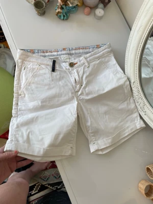Hansen&jakob  bomullsshorts med uppvik - Snygga vita shorts från Gant i bomull med klassisk passform och uppvikta benslut. Shortsen har fickor fram och bak, bälteshällor och stängs med knapp och dragkedja. Perfekta för en fräsch och stilren look i sommar.