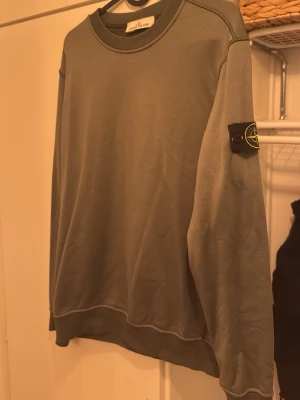 Grön sweatshirt från Stone Island - Snygg grön sweatshirt från Stone Island med klassisk logotyp-patch på vänster ärm. Tröjan har rund halsringning, ribbade muddar och är tillverkad i mjukt bomullsmaterial. Perfekt för en avslappnad streetwear-look.