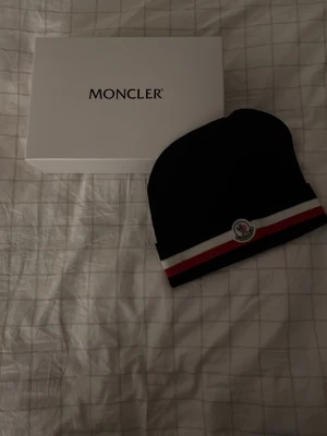 Moncler mössa - Svart moncler mössa väldigt snygg, oanvänd med prislapp. Kommer med låda och allt annat med på bilderna, skön och har tjockt material!