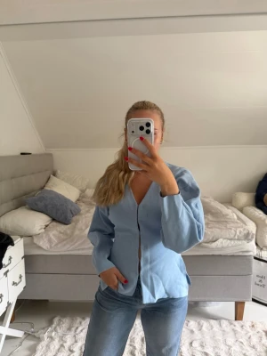 Ljusblå blus från Zara - Snygg ljusblå blus från Zara med v-ringning och knappar framtill. Blusen har långärmade puffärmar och är tillverkad i ett mjukt, stickat material som ger en avslappnad men ändå chic look. Perfekt att matcha med jeans eller kjol. Köpte den för 600kr 