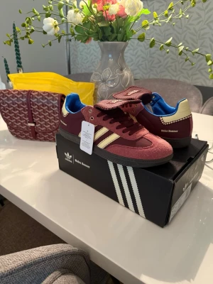 Adidas Wales Bonner vinröda sneakers - Säljer ett par Adidas Wales Bonner sneakers i vinrött mocka och textil med beigea detaljer och blå insida. Klassisk låg modell med bred plös och ikoniska tre ränder på sidan. Snygg retrostil och unika detaljer som sticker ut.