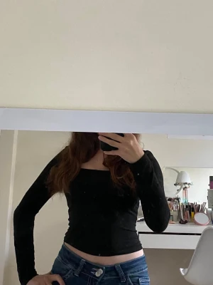 Svart långärmad topp  - En svart långärmad topp med snygg fyrkantig ringning. Modellen är figurnära och toppen är tillverkad i ett stretchigt material som känns mjukt mot huden. Perfekt att styla med jeans eller kjol för en trendig look.