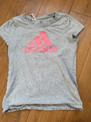 Grå adidas T-shirt  - Grå adidas tröja med rosa logga i barnstorlek 164