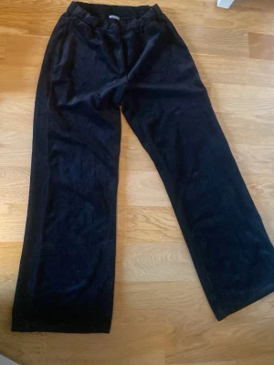 Svarta mjukisbyxor i velour - Säljer ett par svarta mjukisbyxor i mjuk velour med breda ben och resår i midjan. Perfekta för chill dagar hemma eller när du vill ha det extra bekvämt. Klassisk modell utan synliga loggor eller detaljer.
