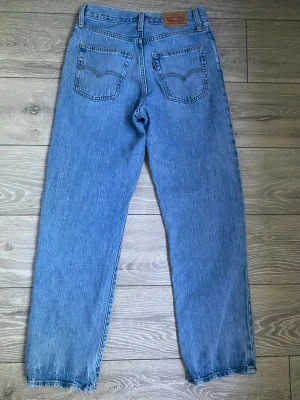 Levi's 94’ baggy ljusblå raka jeans - Klassiska Levi's 94 baggy jeans i ljusblå denim med raka ben och hög midja. Femficksmodell med knappgylf och ikoniska bakfickor med söm. Perfekta för en avslappnad och tidlös stil. Tillverkade i 100% bomull. Strl 26” passar mig som har 27” då jag ville ha tightare passform