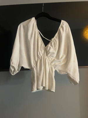 Vit v-ringad blus från Zara  - Snygg vit omlottblus med djup v-ringning och knytband i ryggen. Blusen har trekvartsärmar och ett luftigt, flowy tyg som ger en avslappnad men trendig look. Perfekt att styla med jeans eller kjol för en cool vibe.