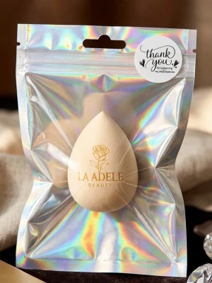 Beige beautyblender från La Adele - En beige droppformad beautyblender från La Adele Beauty. Perfekt för att applicera foundation och concealer jämnt. Tillverkad i mjukt, flexibelt material som ger en naturlig finish. Kommer i en holografisk förpackning med elegant logga.