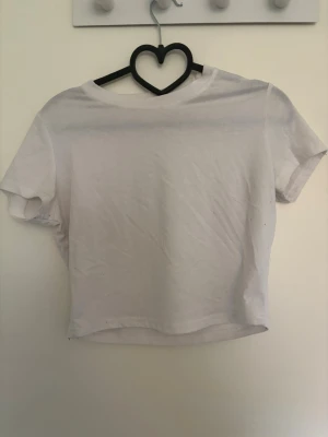 Vit croppad t-shirt - En enkel vit croppad t-shirt med korta ärmar och rund hals. Perfekt basplagg som passar till det mesta och är lätt att styla. Tillverkad i mjukt material för en bekväm känsla. Finns rn likadan fast i svart i min profil