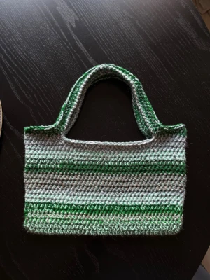 Grön- och grårandig virkad handväska - Virkad handväska med gröna och gråa ränder. Rektangulär form med två korta handtag, perfekt för att bära det viktigaste. Unik och trendig accessoar för dig som gillar virkat och handgjort. 