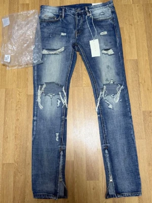 Säljer ett par MNML Ripped Jeans Blue – Size W32 - Jeansen är helt nya och endast testade. Inga skador eller slitage.  Trendiga jeans med ripped design, detaljerade slitningar och dragkedjor vid anklarna – perfekt för en modern streetwear-look. Original tags medföljer.  Size: W32 🏷️ Rabatt vid köp av flera plagg!