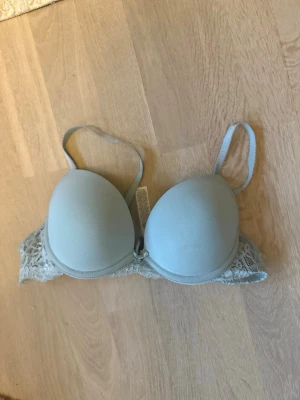 Ljusblå push-up bh med spets - Säljer en ljusblå push-up bh med vadderade kupor och justerbara axelband. Bh:n har fina spetsdetaljer på sidorna och bak, samt en liten rosett framtill. Perfekt för dig som vill ha både komfort och snygg design. Köpte den på Vinted men den var för liten så säljer den här.