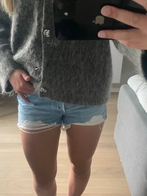 Ljusblå Levishorts med fransig kant - Säljer ett par ljusblå denimshorts med fransig kant och slitna detaljer. Klassisk femficksmodell med knapp och dragkedja framtill. Perfekta för varma dagar och ger en avslappnad look. Aldrig använda och skriv för fler frågor!💞