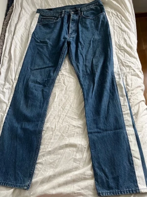 Blå raka jeans i klassisk modell - Säljer ett par blå jeans med rak passform och hög midja. Jeansen har fem fickor, dragkedja och knapp i gylfen. Tillverkade i kraftigt denimtyg som ger en tidlös look. Perfekta till en avslappnad stil och funkar året runt.