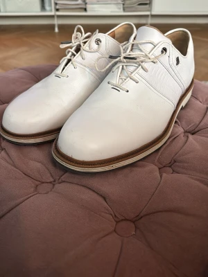 FootJoy golfskor vit - Storlek:42 bredd: wide. Snygga vita golfskor från FootJoy med klassisk snörning och greppvänlig sula med dobbar. Skorna är tillverkade i slätt och strukturerat läder med diskreta detaljer och kontrastfärgad sula. Perfekta för dig som vill ha stilrena skor på golfbanan. 