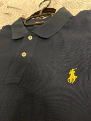 Marinblå pikétröja från Polo Ralph Lauren - Klassisk marinblå pikétröja från Polo Ralph Lauren med gul broderad logga på bröstet. Custom Slimfit L