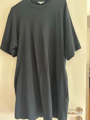 Svart oversized t-shirt från COS - En svart oversized t-shirt från COS i mjuk bomull. Klassisk rund halsringning och korta ärmar. Perfekt för en avslappnad och stilren look. Passar dig som gillar minimalistisk design och bekväma plagg. Märket COS