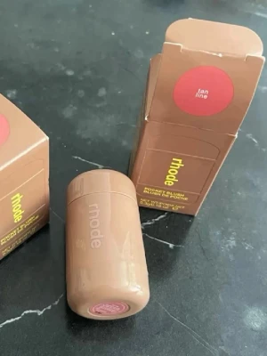 Rhode Pocket Blush Tan Line - Rhode Pocket Blush i färgen Tan Line är ett krämrouge i en smidig stickform. Färgen är en varm, naturlig nude-brun ton som ger kinderna en fräsch glow. Förpackningen är kompakt och beige med modern design, perfekt att ha med i väskan.