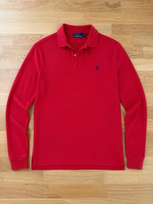Polo Ralph lauren pike (långärmad) - 🔴 Polo Ralph Lauren långärmad pikétröja – Röd • Klassisk långärmad pikétröja från Polo Ralph Lauren • Stilren röd färg med mörkblå broderad logotyp på bröstet • Tillverkad i mjuk och bekväm bomullspiké • Klassisk krage med knappslå • Ribbstickade muddar vid ärmsluten • Normal passform som passar både vardag och mer uppklädda tillfällen • Tidlös modell som aldrig går ur stil • Perfekt att bära året runt, ensam eller under en jacka Skick • Fint begagnat skick • Inga större anmärkningar • Nytvättad