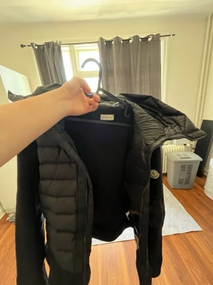 Svart pufferjacka från Moncler - Säljer en svart pufferjacka från Moncler med huva och dragkedja. Jackan har Moncler-logga på ärmen, quiltad design och sidofickor. Perfekt för kalla dagar och riktigt snygg till streetwear-stilen. Nfc funkar perfekt