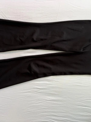 Svarta utsvängda leggings - Säljer ett par svarta leggings med utsvängda ben. De har en enkel och stilren design utan synliga detaljer eller loggor. Materialet ser stretchigt och mjukt ut, perfekt för en bekväm och snygg look. Lite slitna mellan låren men inget som påverkar funktionaliteten på byxorna. Köpare står för frakt. 