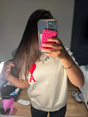 Vit stickad topp från Ami Paris - Vit stickad topp från Ami Paris med korta ärmar och ribbade kanter. På bröstet finns ett rött hjärta med bokstaven A. Perfekt för dig som gillar stilrena plagg med en twist. Helt ny!