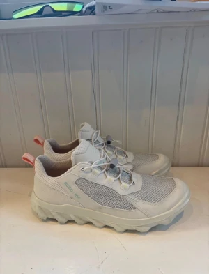 Beige sneakers från ECCO MX - Snygga beige sneakers från ECCO MX med meshpaneler och robust sula. Skorna har elastiska snören med snabblås och orange detaljer på hälen. Perfekta för dig som gillar en sportig och modern look.