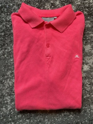 Rosa pikétröja från J.Lindeberg - Säljer en klassisk rosa pikétröja från J.Lindeberg med liten vit logga på bröstet. Tröjan har krage, knappslå med en knapp och är gjord i bomull. Perfekt för en stilren och sportig look. Storlek Xs. Bra skick